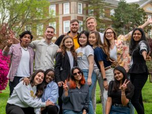 A group of students of different ethnicities smile for the camera on campus.