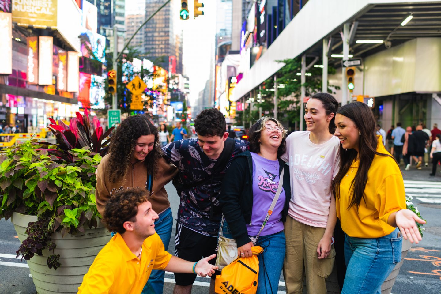Casually dressed young adults are laughing and smiling at one another in Times Square with colorful billboards, bright lights and skyscrapers in the background