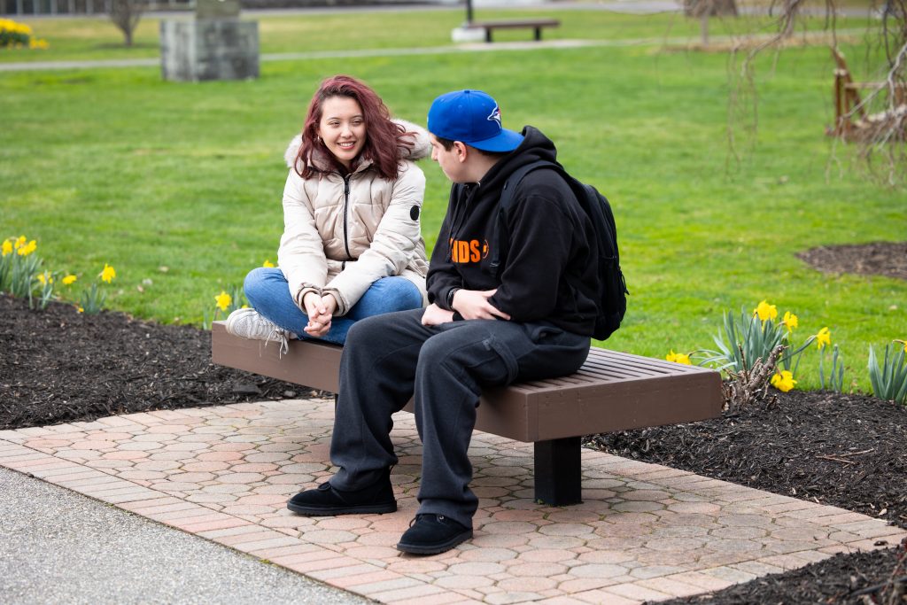 Two students talking together on a bench on Adelphi's campus