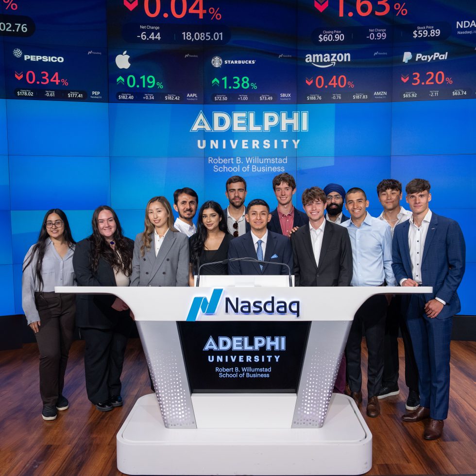 Adelphi students stand in Time Square in New York City in front of the Nasdaq with the Adelphi University Logo displayed on the large screen.