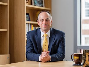 Dr. Kline, dressed in business attire, at his desk, looking at the camera. 