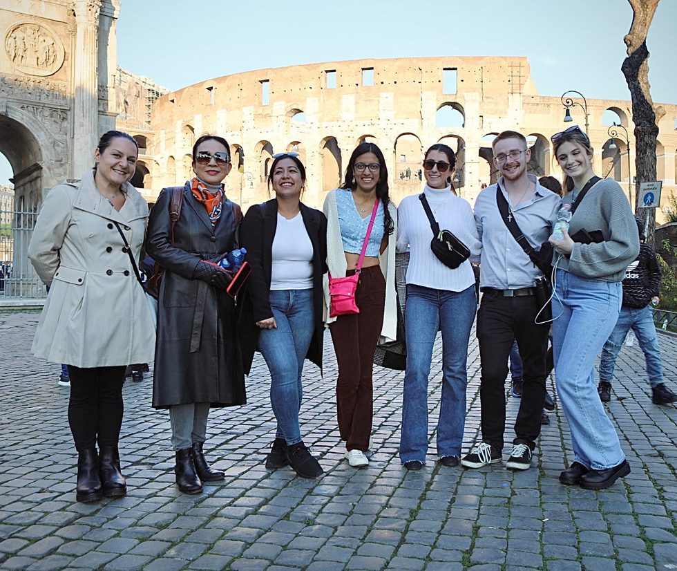 Dean Xiao-lei Wang standing with Adelphi students in front of a Roman Coliseum in Italy.