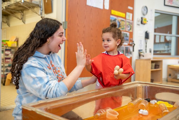 Adelphi University Early Learning Center - Adelphi students high-fives a child during sensory play.