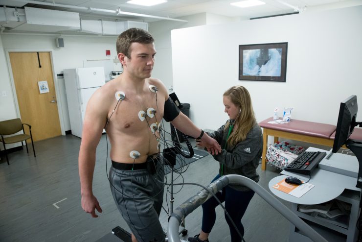 Exercise Science Lab - A student walks on a treadmill with monitors on his chest to track data.