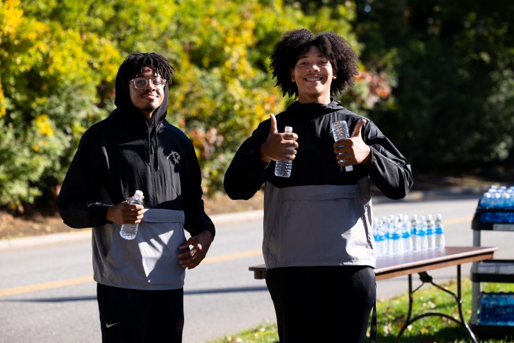 Two Adelphi students working a 5K run on campus handing out water to participants. 