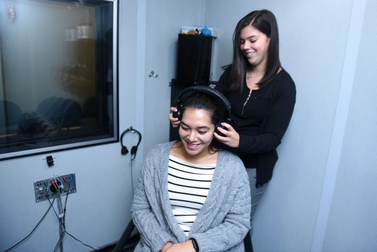 Audiology assessment at the Hy Weinberg Center. Student places headphones over a patient's ears.