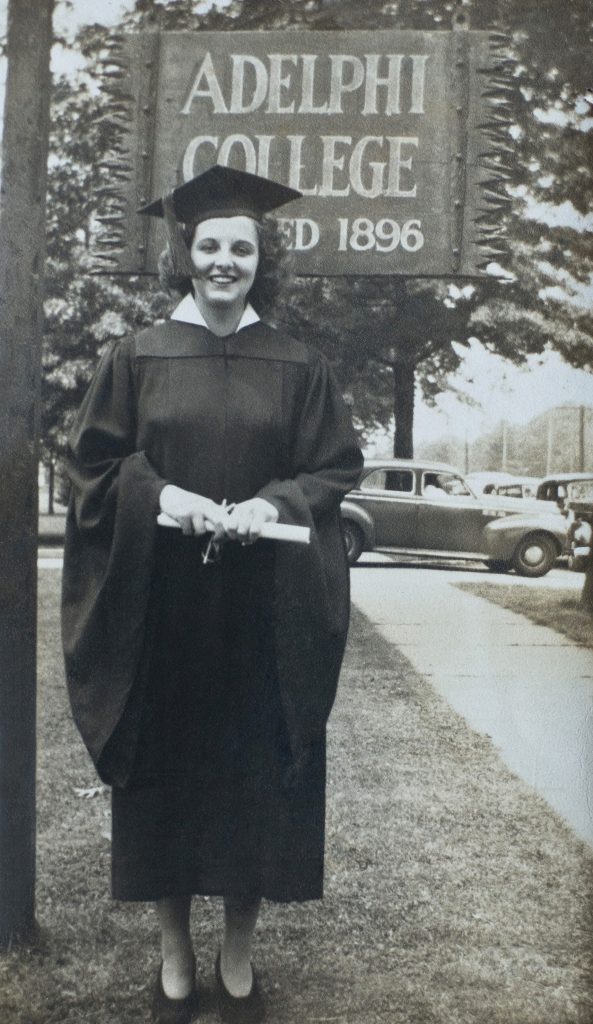 Ruth Woodroffe Gangel in her academic regalia standing in front of an Adelphi College established in 1896 sign.