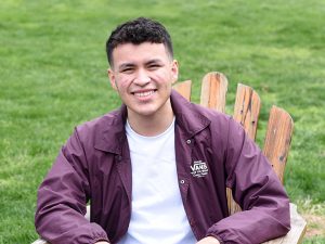 Headshot of young man sitting outside smiling at camera