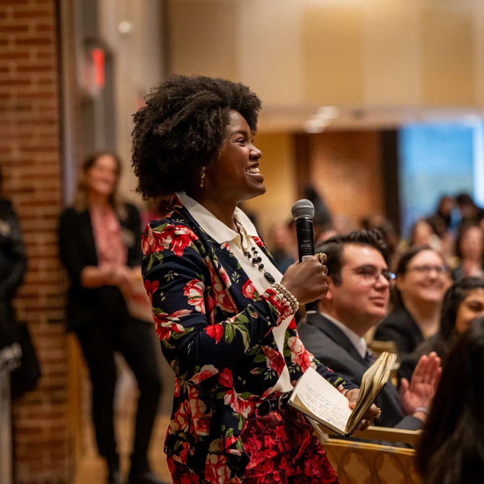 A confident Black women holding a microphone laughing during the Women's Leadership Conference at Adelphi University