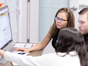 Professor Lukic and two students in front of a large computer screen on a table.