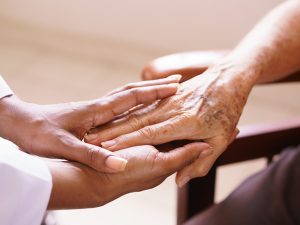 A patient's hand enveloped by the two hands of someone comforting her.