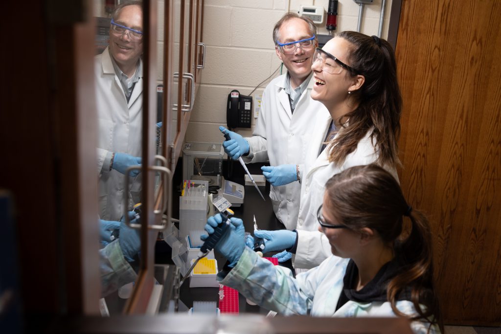 Professor Brian Stockman, PhD working with students in the lab. They're enjoying themselves, breaking into laughter.