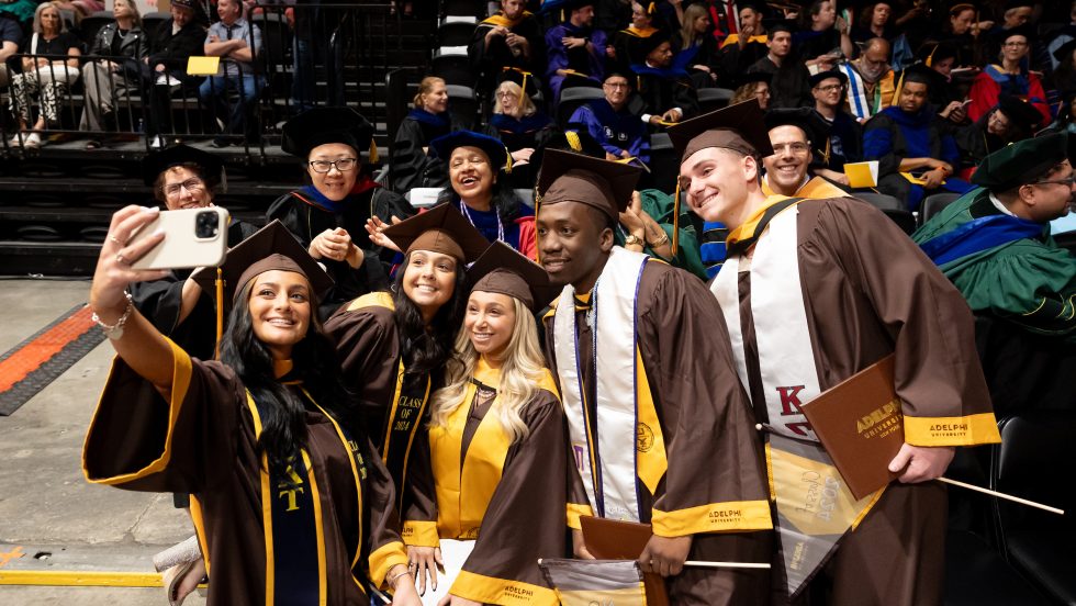  A group of five graduates posing with faculty at Adelphi's 2024 Commencement ceremony.