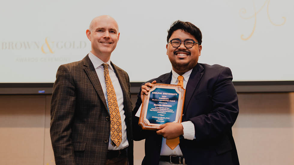 Man stands next to young man with glasses, who is holding up a plaque