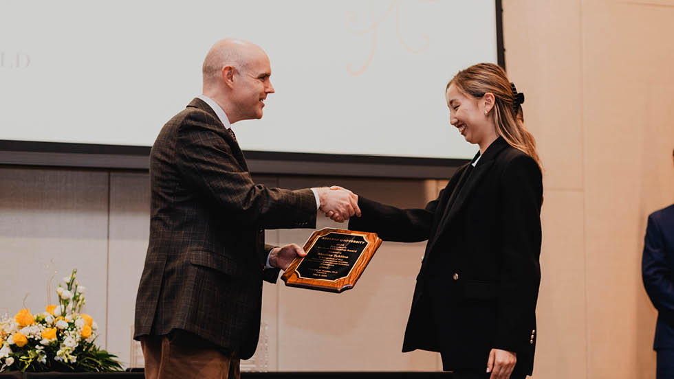 Man shakes hand of young woman as he hands her a plaque