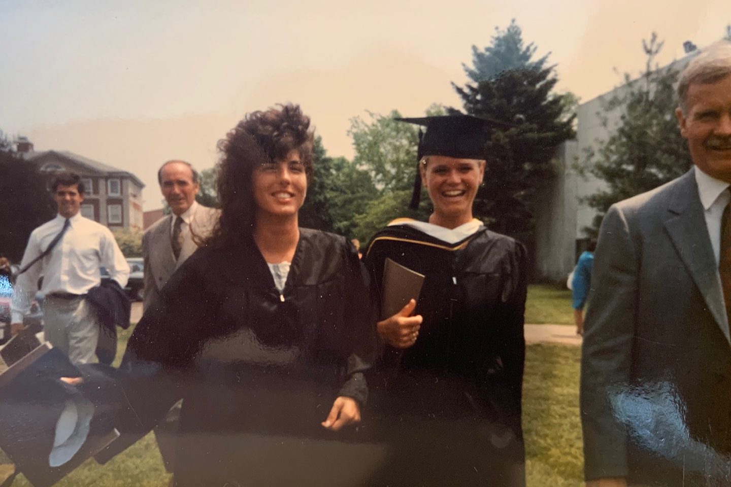 Two women in graduation attire, half of man seen off to the right