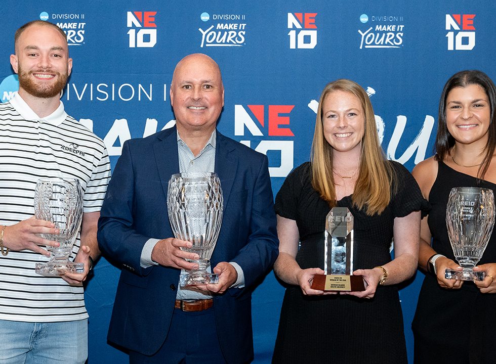Adelphi student-athletes and athletic director holding NE10 Presidents’ Cups and Woman of the Year trophy.