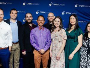 Eight people in formal attire stand in front of a blue backdrop that reads "Opera Omaha."
