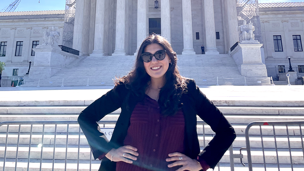 Young woman stands with hands on hips in front of large white pillared building.