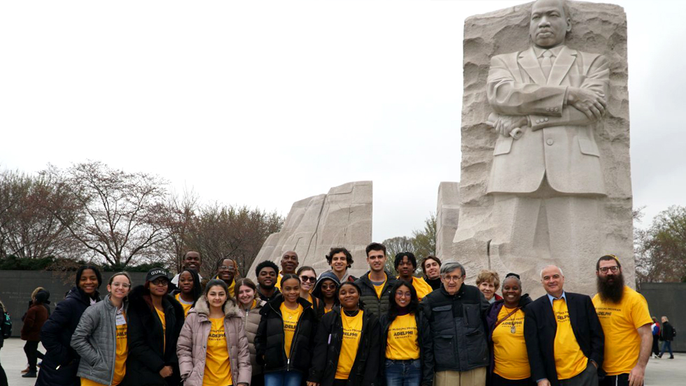Two lines of people standing in front of a statue of a Black man