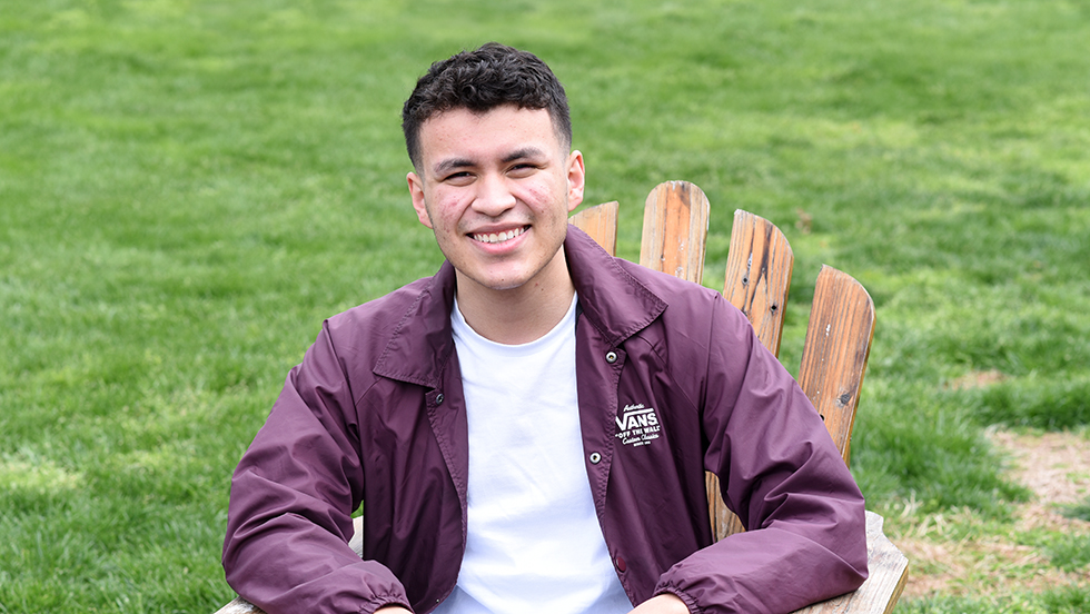 Headshot of young man sitting outside smiling at camera