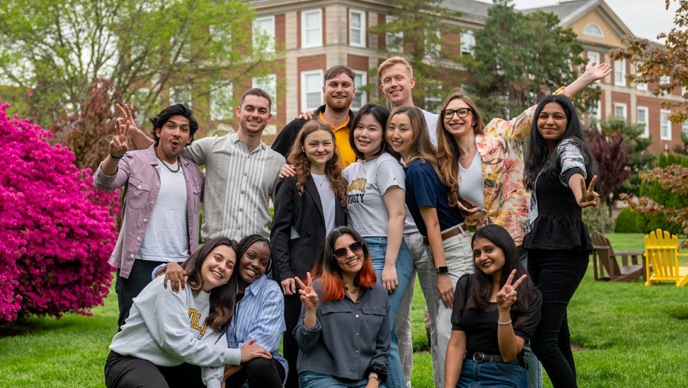 A group of students of different ethnicities smile for the camera on campus.