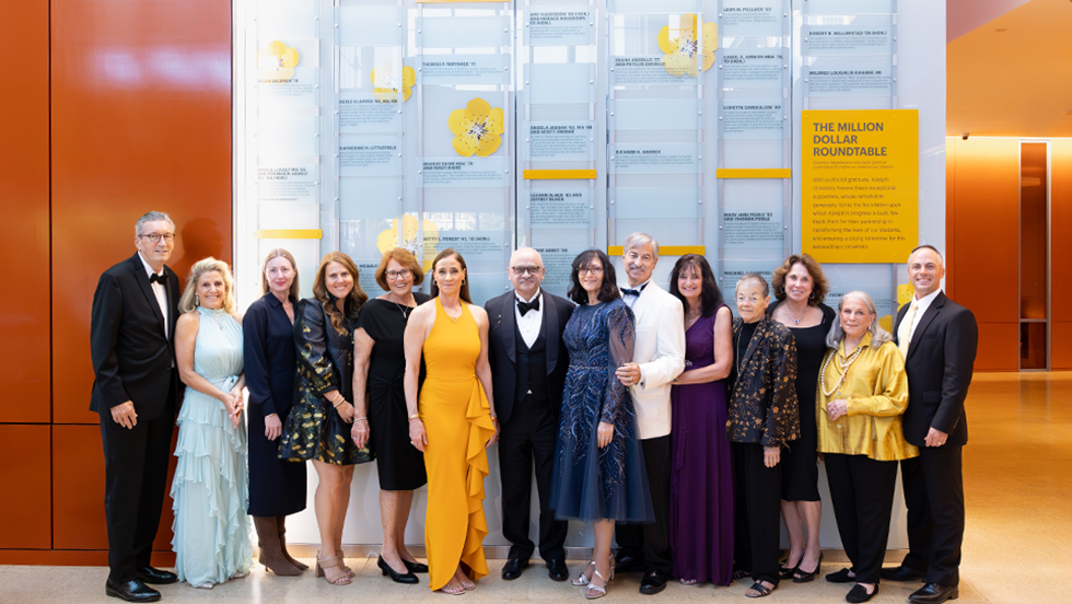 Members of the Adelphi University Million Dollar Roundtable pose in front of the wall honoring them and the University’s other top benefactors. 