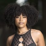 A young Black woman with an Afro hairdo, wearing hoop earrings and a sleeveless black cutout dress