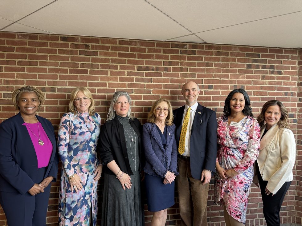 A group of women and one man smiling in front of a brick wall.