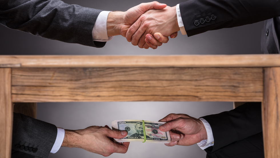 Two images: Above, the outstretched arms of two men in business suits, shaking hands. Below, the same two arms, this time passing a stack of $50 bills.