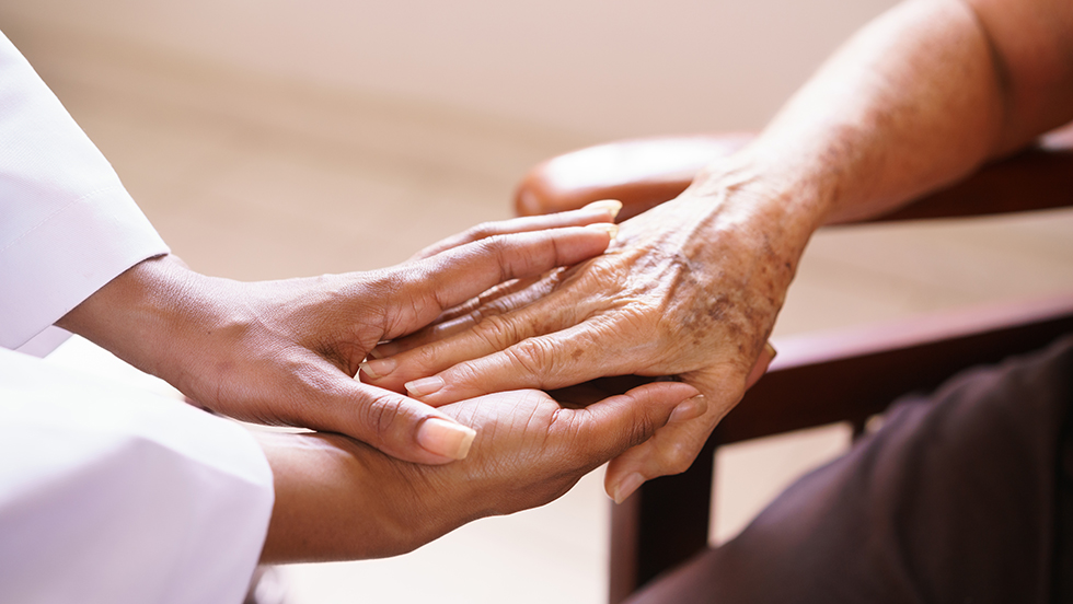 A patient's hand enveloped by the two hands of someone comforting her.