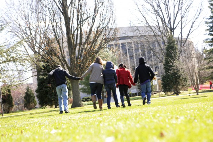 Group of students holding hands and running towards a building