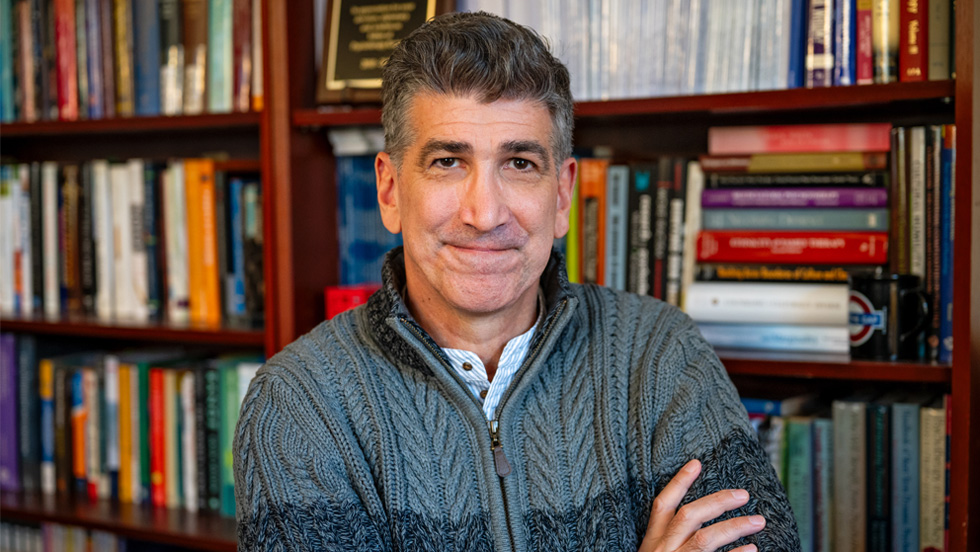 A man, smiling with arms crossed, in front of bookcase