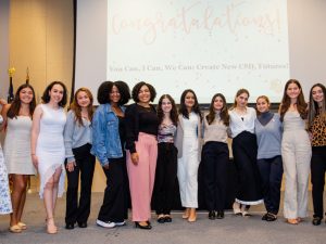 Fourteen young women stand on a stage for a group photo. The screen behind them reads: "Congratulations! You Can, I Can, We Can, Create New CSD Futures!”