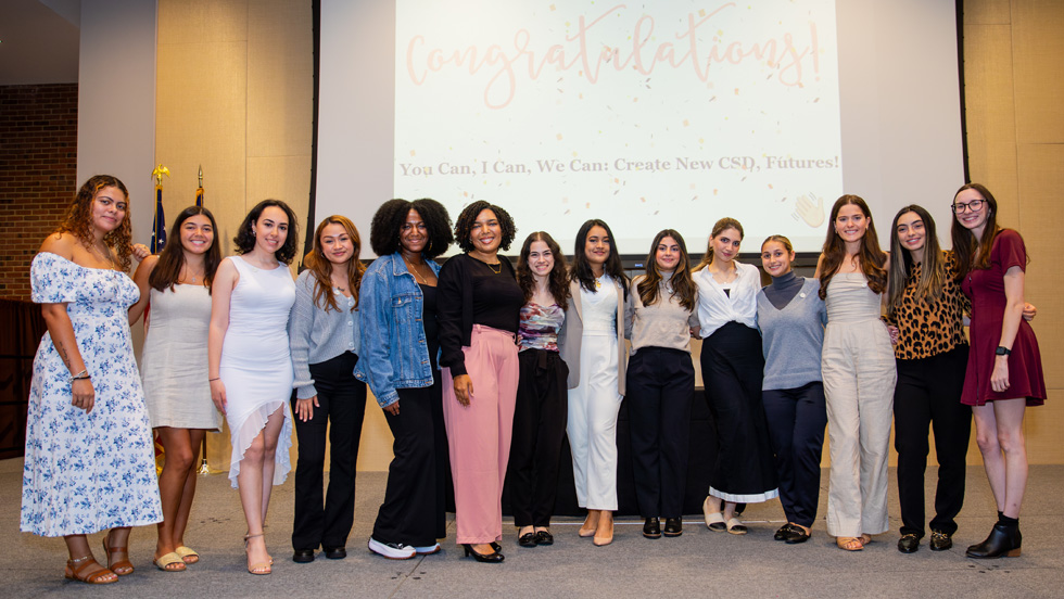 Fourteen young women stand on a stage for a group photo. The screen behind them reads: "Congratulations! You Can, I Can, We Can, Create New CSD Futures!”