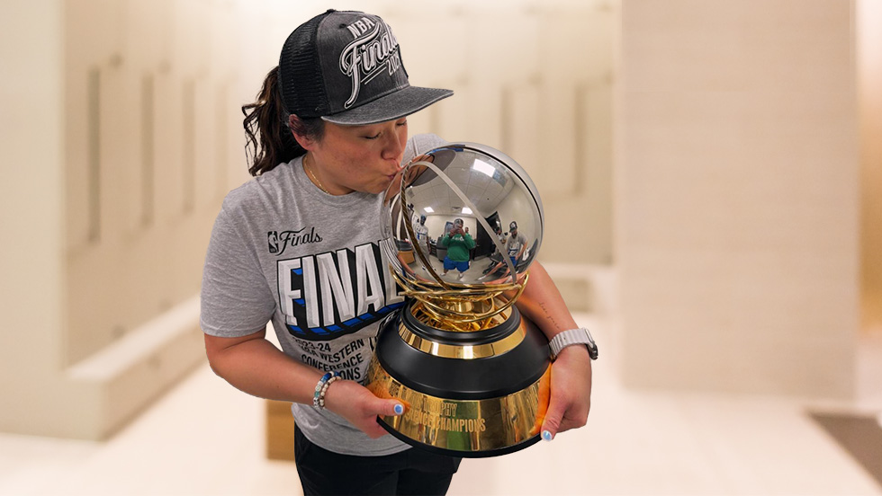 Heather Mau in the team's training room kissing the championship trophy, which she holds in her arms.  The trophy is a silver basketball on a wood pedestal with gold plating.  She is wearing a t-shirt and hat given the players and training staff commemorating the Western Conference championship.