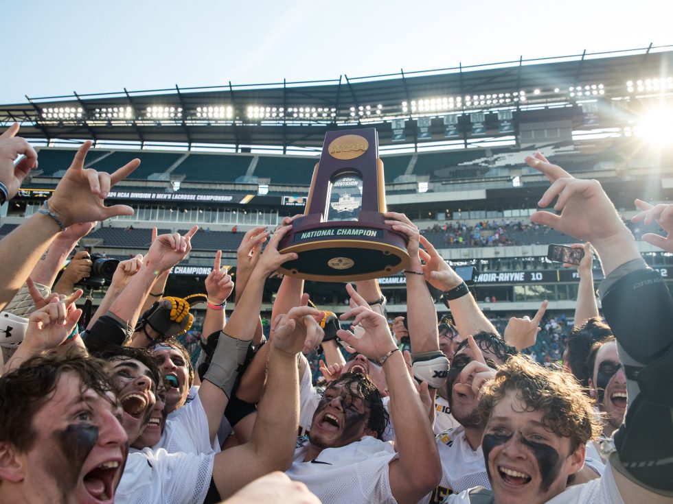 Men’s lacrosse players running across the field in celebration of their win