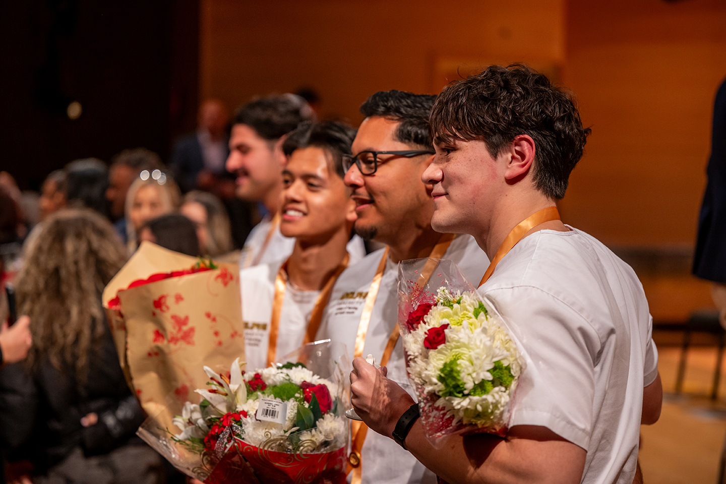 Students in nursing coats smile and put their arms around each other as they hold bouquets of flowers.