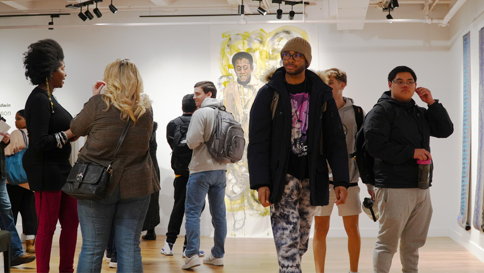 Students mingle at the Ruth S. Harley University Center Gallery, with a large sketch of James Baldwin in the background.