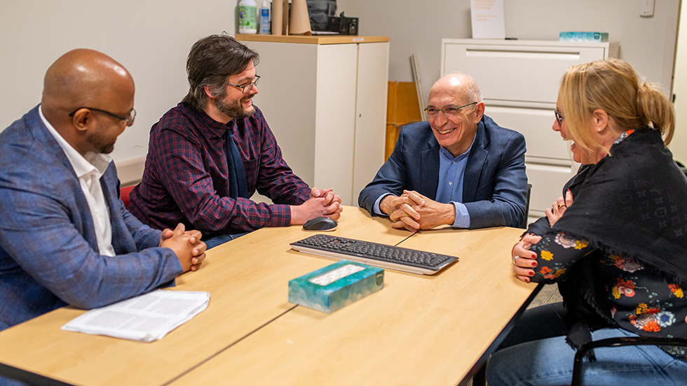 A faculty member and three adult students sit around a small table, talking and smiling.