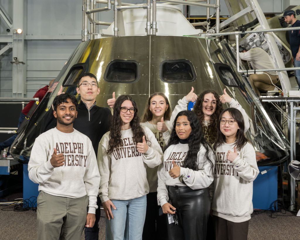 Students and professor posing in front of a mockup of the Orion spacecraft.