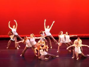 Dancers on a stage with a red backdrop. 