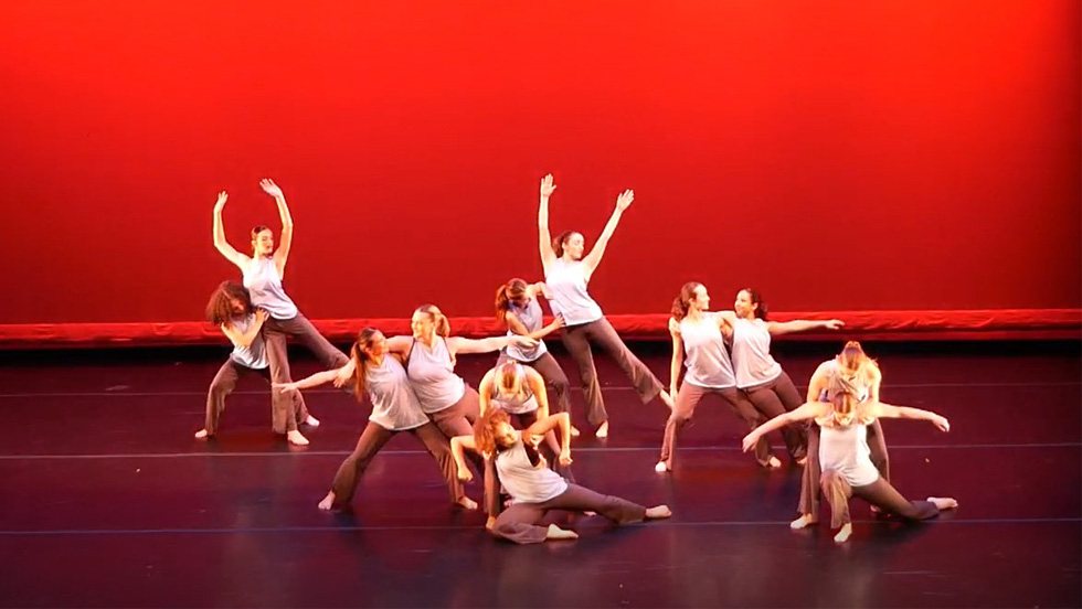 Dancers on a stage with a red backdrop. 